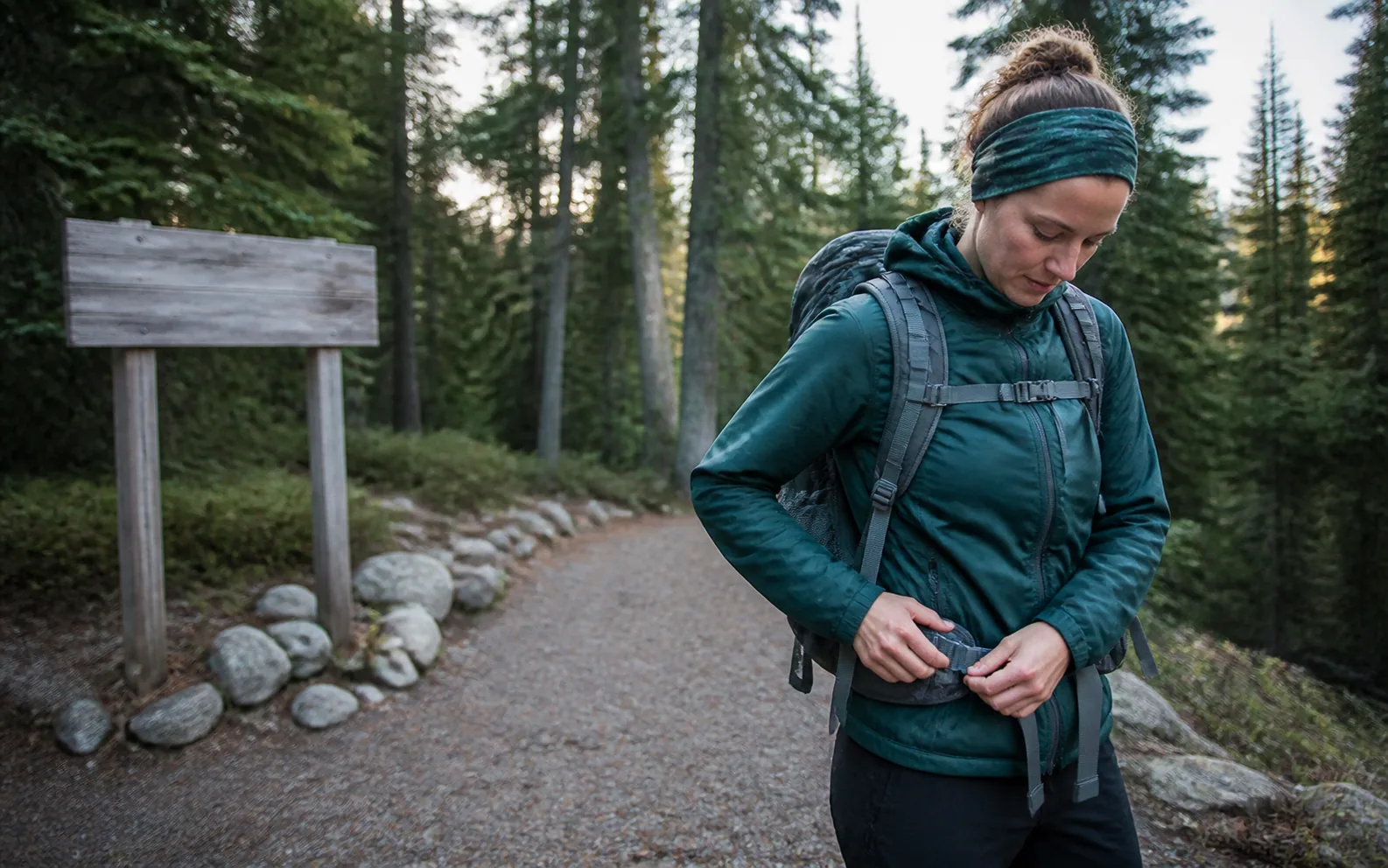 A hiker tightening a compact daypack beside a forest trail before a morning hike.