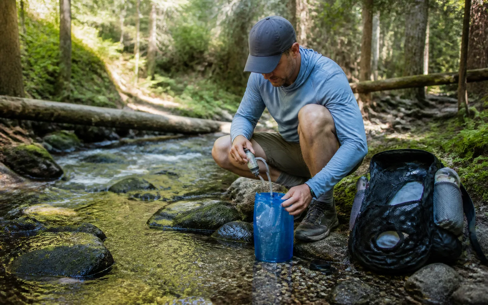 A backpacker collecting and filtering clear stream water into a bottle near camp.