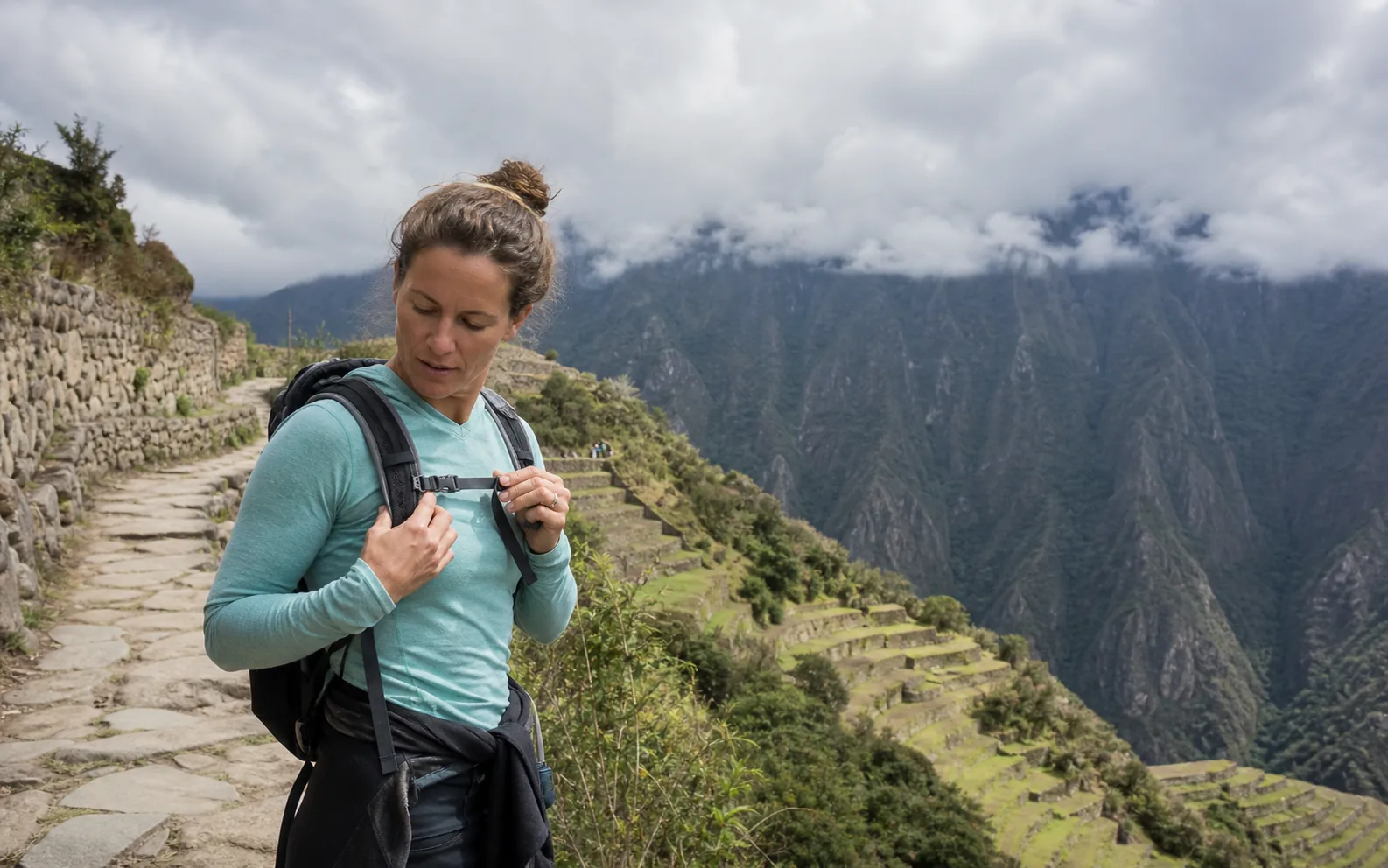 A guided trekker pausing to adjust a small daypack on a high Andean stone path.