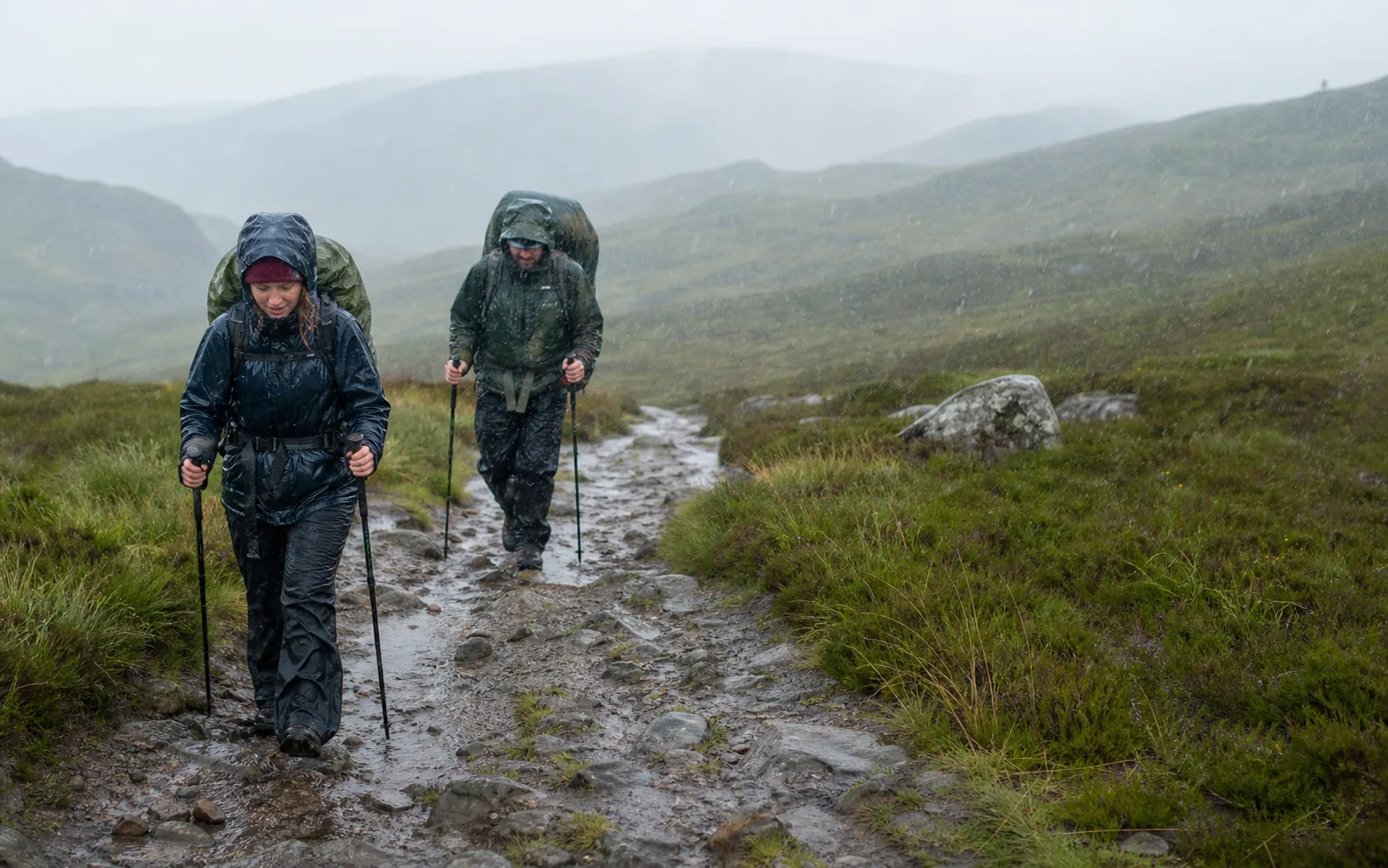 A walker in rain gear crossing open Scottish moorland on the West Highland Way.